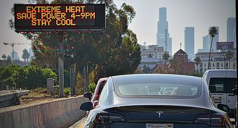 A Tesla electric car is driven past a sign warning of extreme heat and the need to save power between 4-9pm. Los Angeles, USA. September 2022.