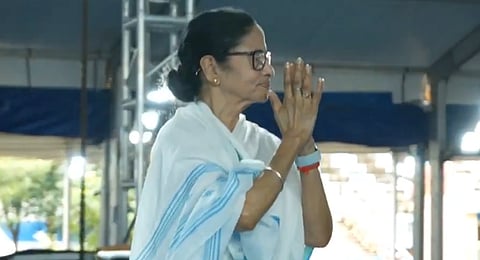 In the imagr Mamata Banerjee is shown joing her hands looking at someone