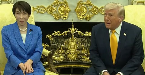 In the image Japan PM Takaichi Sanae is sitting in a blue suit with her hands crossed. she is sitting right next to President Donald trump at the White House.