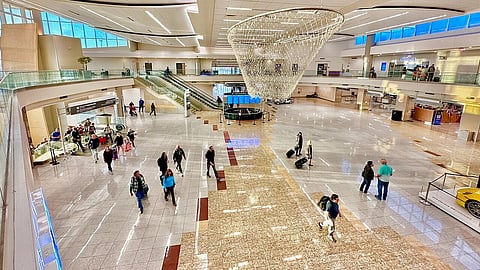 A brightly-lit lobby with a tiled foor, escalators, a hanging decoration and people walking