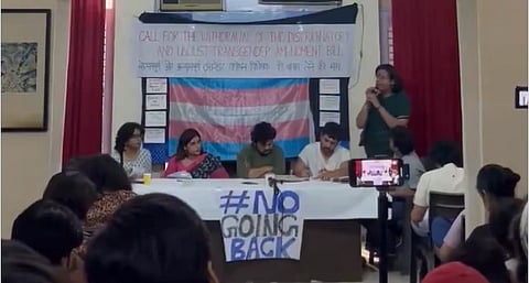 A panel of five people sits at a table with a "#No Going Back" sign. Behind them is a large transgender flag and a banner protesting a bill.