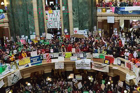 Many protestors stand on two levels with 'tax the rich' posters