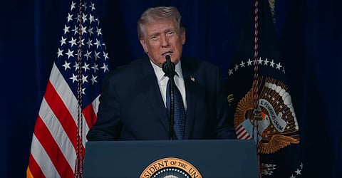 In the image President Donald Trump is shown adressing the people in a podium behind him are US Flags