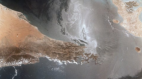 Satellite image showing the Strait of Hormuz, with arid desert landscapes on either side and dark blue waters in the center, under a clear sky.