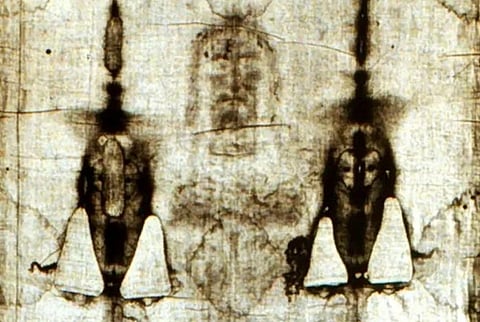 A sepia-toned image of the Shroud of Turin, showing faint outlines and shadows of a man's face and body, evoking mystery and solemnity.