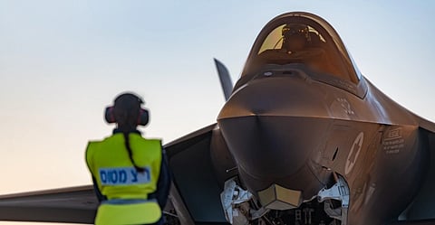 Imag eif Israeli Air Force F-35I Adir, Operation Roaring Lion 2026
A person in a reflective vest and earmuffs observes a parked fighter jet at dusk. The aircraft's cockpit is highlighted against a soft evening sky.