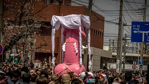 In the image many people are shown carrying a giant penis inside a shrine of pink colour