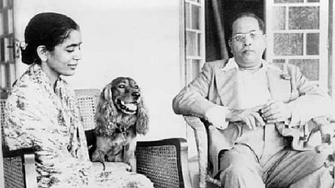 Babasaheb and Savita Ambedkar sitting next to each other in wicker chairs with a dog between them