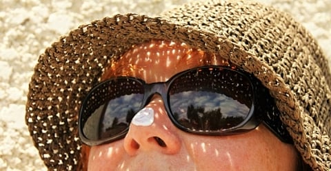 A woman's face above upper lips, wearing sunglasses and a hat, protecting her from UV rays