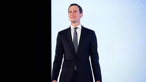 Jared Kushner in a black suit standing in front of a black and white background