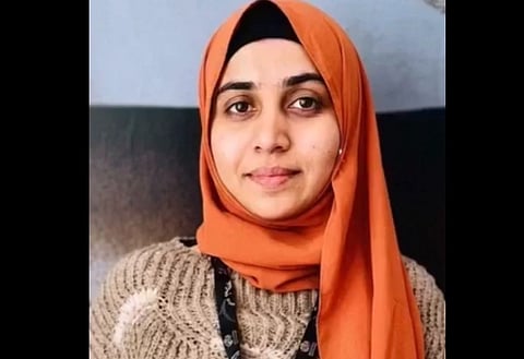 Image of Nida Khan wearing a burnt orange hijab and beige knit sweater, smiling softly at the camera.
