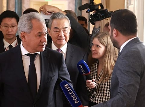 Image of Wang Yi, surrounded by group of people, walk through a corridor. Reporters with microphones and a camera crew surround them, capturing the scene.