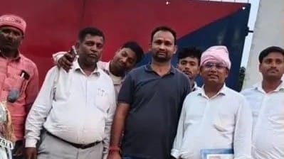 In the image one person is shown in black with many other posing for a picture outside a police station
