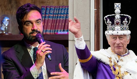 A man in a suit speaks into a microphone beside a shelf of books. To the right, a person dressed as royalty waves, wearing a purple robe and ornate crown.