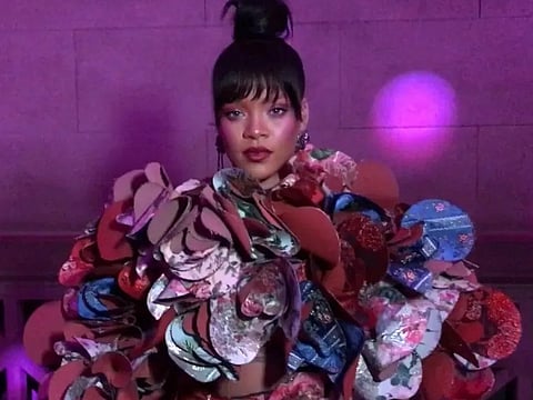 Image of Rihanna at Met Gala 2017 in an elaborate floral and geometric dress stands against a purple-lit background, exuding a bold and artistic aura.