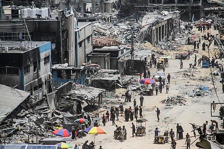A alley is war zone of gaza. buildings are shown half destroyed with people walking on the street