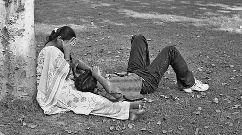 black and white photo of an indian couple sitting in a park, covering their faces