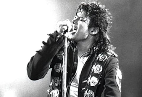 Singer passionately performing on stage, leaning into a microphone. Dressed in a decorative jacket, the scene captures intense emotion and energy.