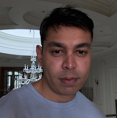Image of Prateek Yadav in a grey shirt behind him is a luxurious background and a chandelier.