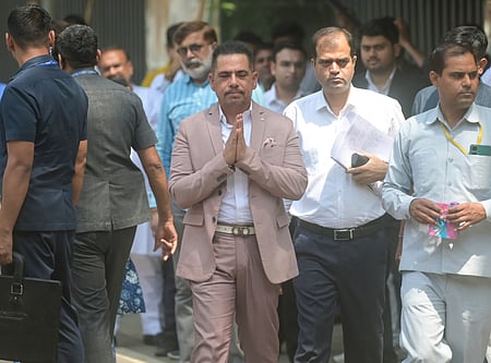 A man in a beige suit walks among a group, hands clasped in greeting. Others wear formal and casual attire. The scene is outdoors and conveys a serious tone.