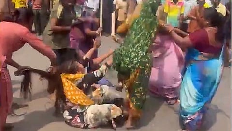 two women sit on the road, while others pull their hair and attack them