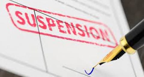 In the image a document is shown with "Suspension" written in it with red paint and a pen is shown writing something