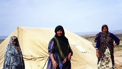 Three Afghani women standing in front of a tent amidst economic fallout of Iran War