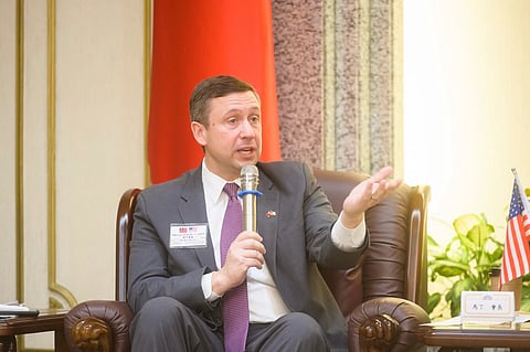 In the image Ken martin is shown with a mic in sofa beside him is america flag in a table