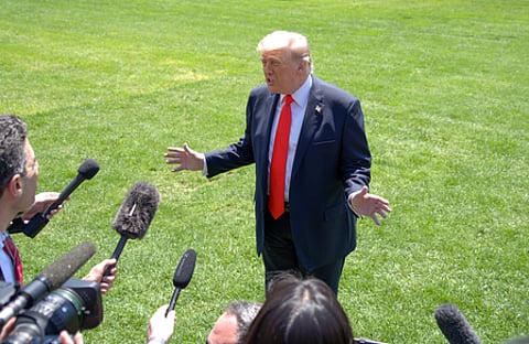 Image of Donald Trump talking to press on a green ground.