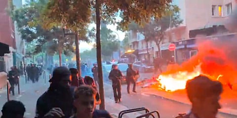 Many people are walking in the street and beside them is a fire blaze