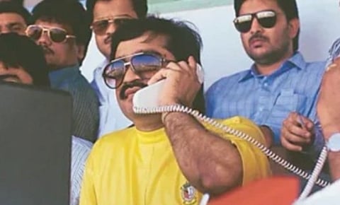 Image of young dawood ibrahim in a yellow t shirt. he is wearing sun glasses and holding a telephone.