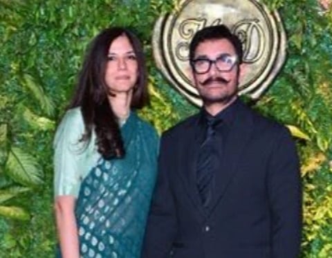 Image of Aamir Khan and Gauri Spratt posing. their background has green leaves behind them.