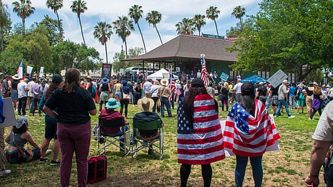 A large group of individuals in a park, waving American flags, celebrating patriotism and community spirit.