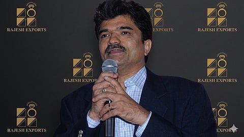 A man in a suit, Rajesh Mehta, holds a microphone while preparing to speak at an event.