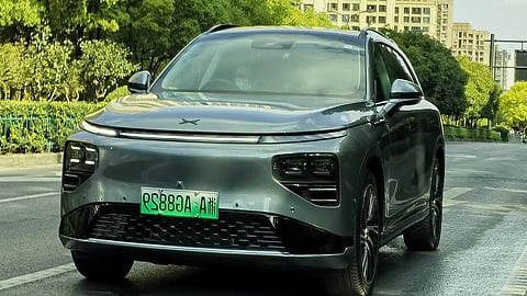 A sleek electric SUV navigates a city street, with urban scenery and people in the background.
