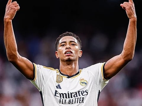 Image of a FIFA football player with both his hands raised up. the background in the image is blurred and is completely focused on him. he is wearing a white Emirates jearsey.