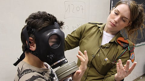 A woman and a young boy, both equipped with gas masks, conveying a theme of protection in a hazardous situation.