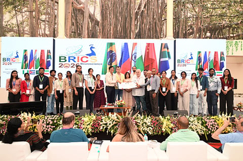 In the image the BRICS 2026 is shown in which many people with i card are shown standing on the stage