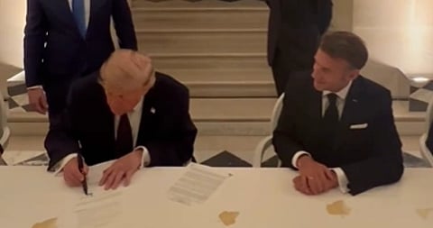 Image of Donald Trump signing US iran deal in France. he is seated next to french president Emmanuel Macron.