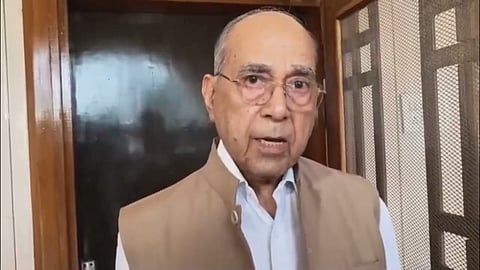 Nripendra Misra speaks to the media outside a home, standing near a door.