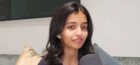 Image of Avni Kejriwal giving an interview with a grey background. She is sitting on a couch.