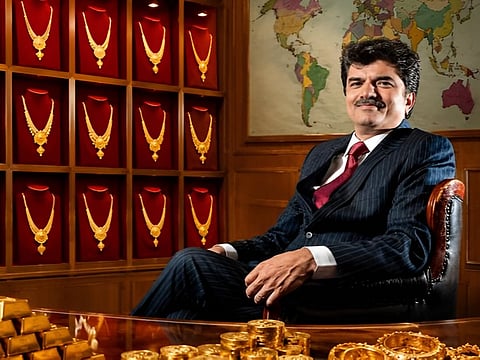 Rajesh Mehta sitting happily on the right wearing suit and red tie, with gold necklaces arranged in the jewelry store on the left.