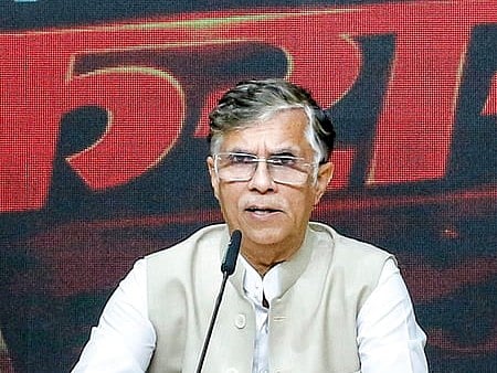 Image of Pawan Khera speaking in front of a mic and addressing agroup of people. he is wearing a formal attire and documents are placed before him.