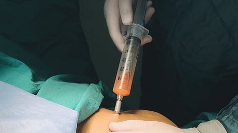 An doctor injecting a syringe into abdomen.