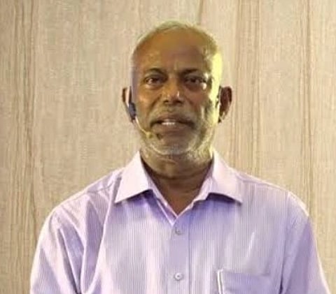 Image of Social worker D Prakash Rao. Padmashri laureate. speaking to people. he is wearing a label mic on his cheek and his hands are crossed