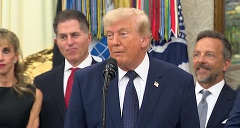 Image of Donald trump speaking in front of a crowd. he is speaking at a official setting and people are around him standing.