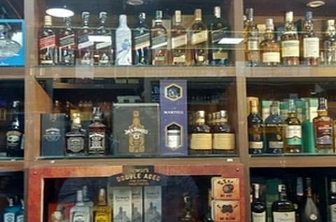 Image of numerous bottles of liquors placed on a wooden shelf with glass doors.