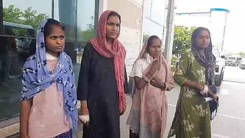 Image of four women standing with their heads covered in shawls. they seem to be standing in front of a gate of a building.