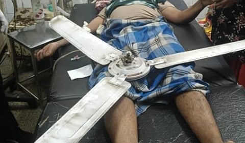 An image of a man laying and a fan is right below his abdomen. he seems to be in a hospital.