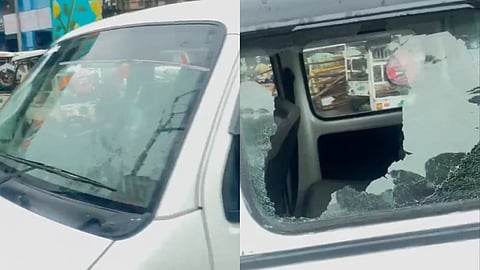A white van with a cracked front windshield and a large hole in the rear side window, parked in an urban area with visible street reflections.